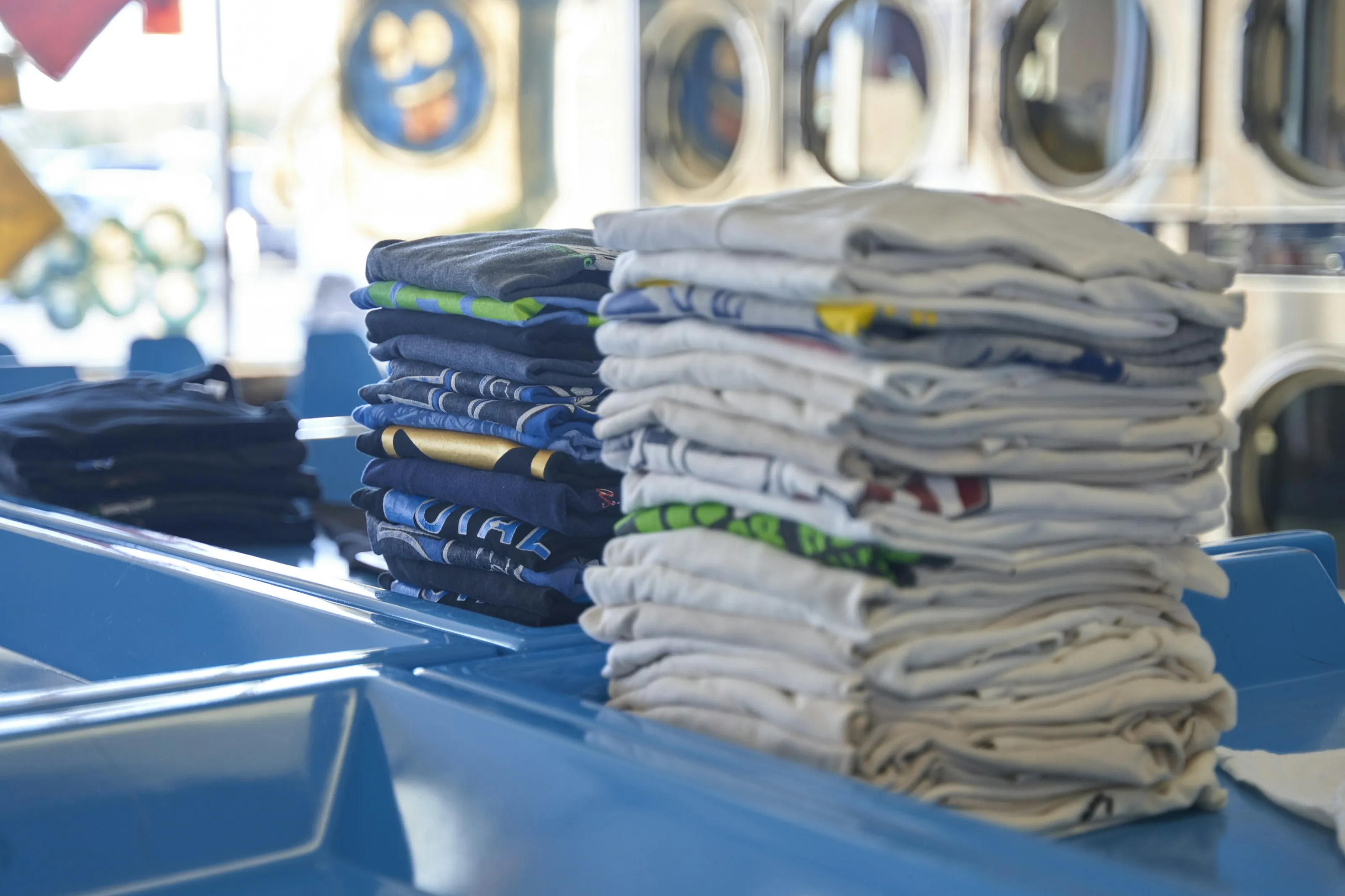 Stacks of freshly folded shirts on a laundromat folding table