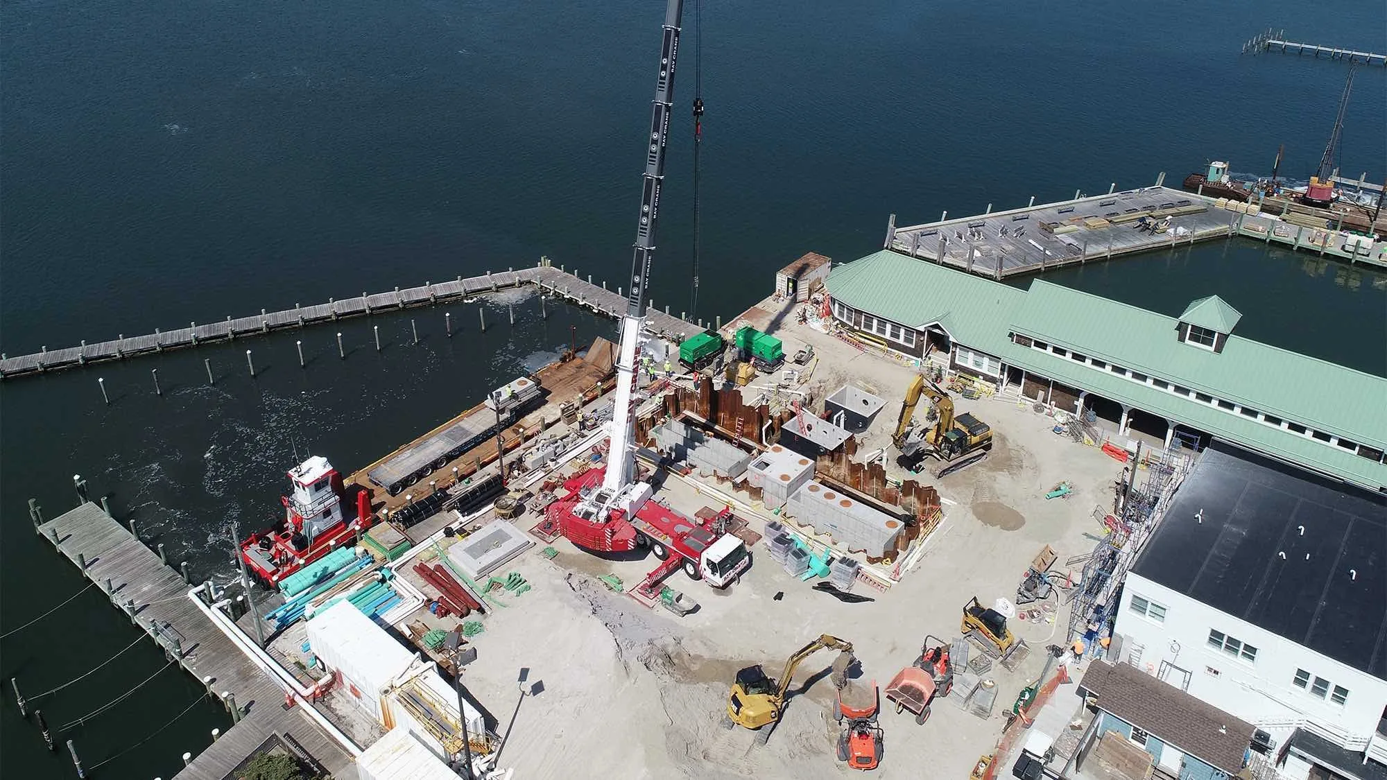 Aerial view of sitework on the Village of Ocean Beach waterfront, with a crane and barge at the dock