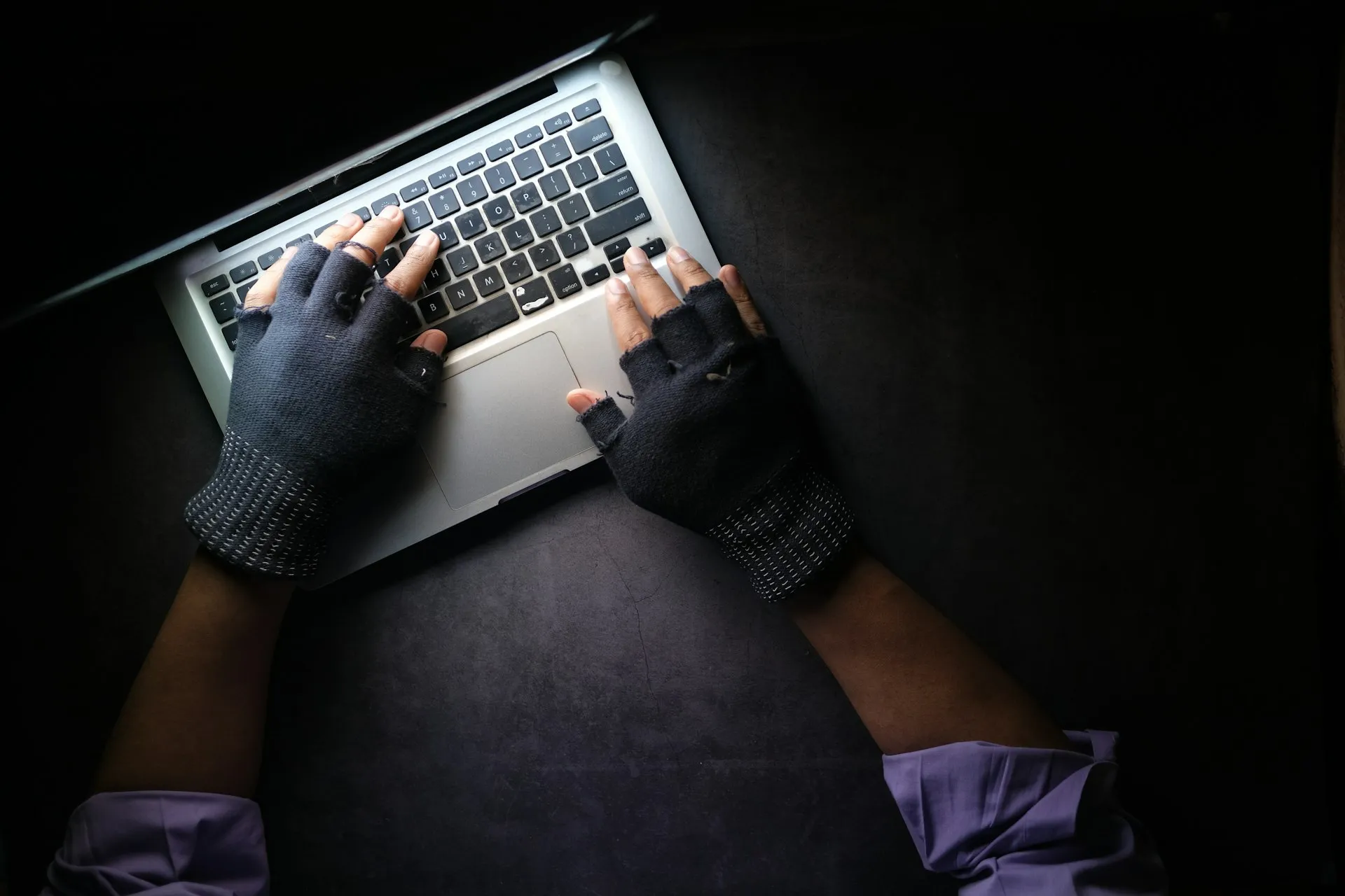 Gloved hands typing on a laptop in the dark