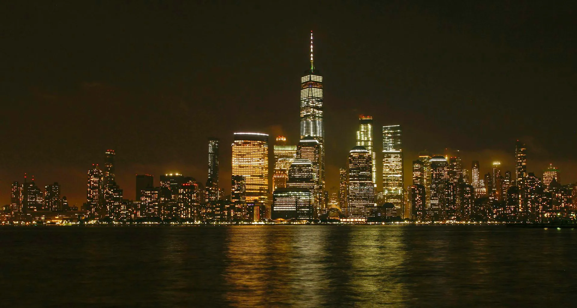Lower Manhattan skyline lit up at night across the Hudson River