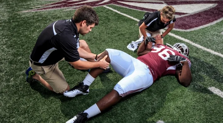 Therapist treating a football player's leg on the field